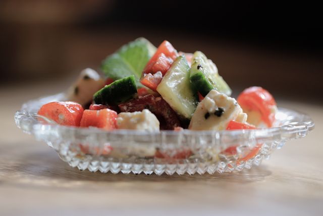 A vibrant mixed salad with feta cheese, cucumbers, and tomatoes in a glass dish.