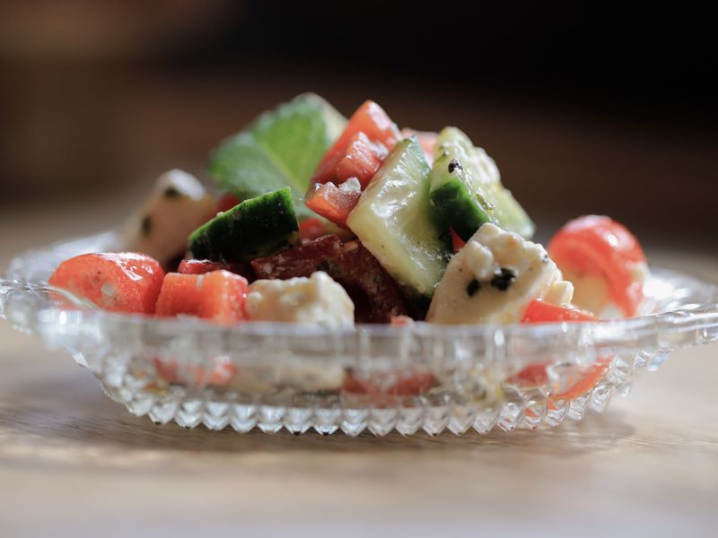 A vibrant mixed salad with feta cheese, cucumbers, and tomatoes in a glass dish.