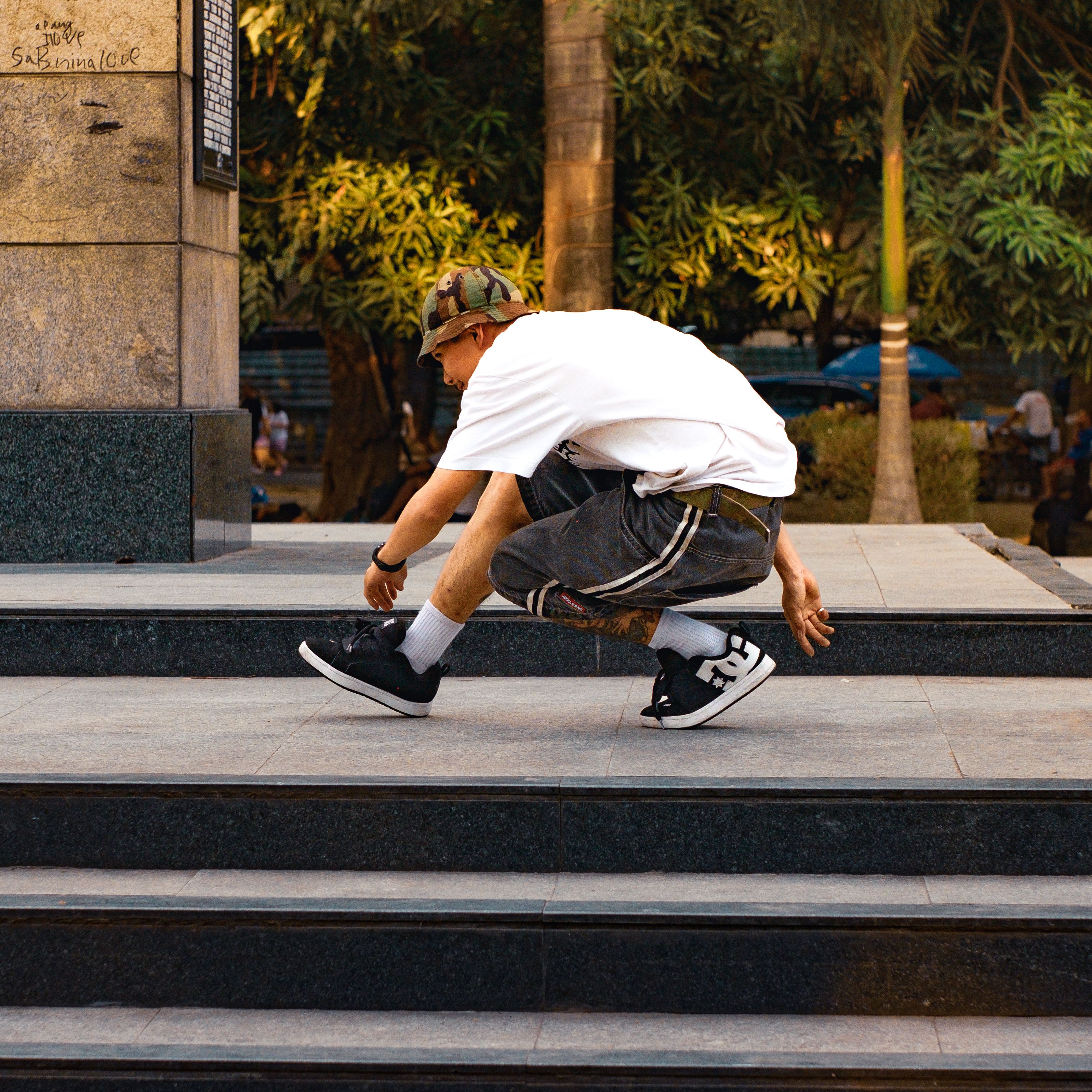 A young skater crouching on urban steps in a park setting. Captures dynamic street culture.