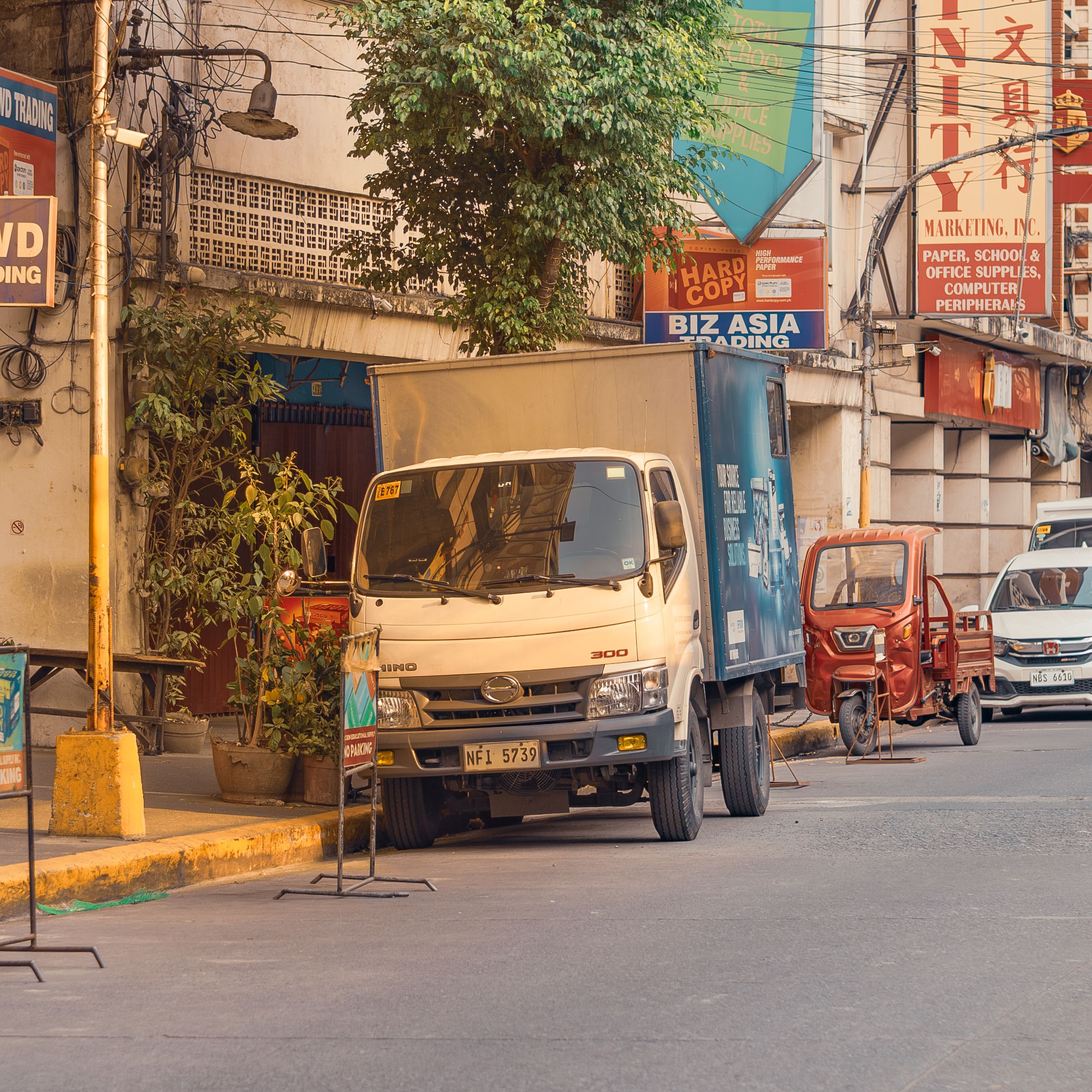 Street view of an urban area with vehicles parked and colorful shop signs. Captures a typical city day.