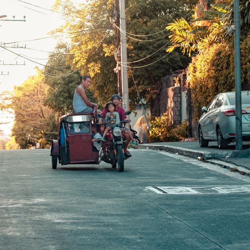 Free A family enjoys a tricycle ride along a sunlit street in Metro Manila, Philippines. Stock Photo