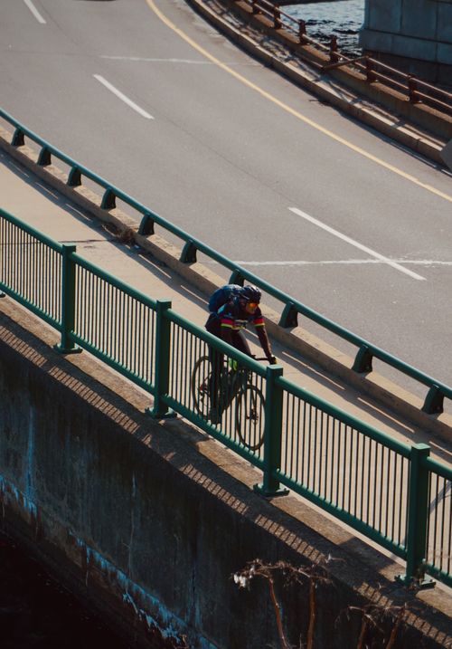 Free A cyclist riding on an urban bridge during the day, showcasing dynamic motion and city scenery. Stock Photo