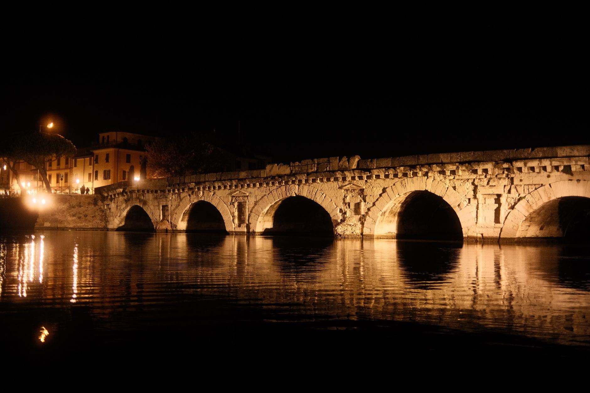 Stunning night view of an ancient Roman bridge in Italy, beautifully lit over calm waters.