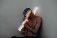 光头男人在彩虹光映照的白墙上纹身，传递着骄傲与内省