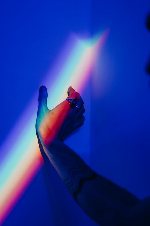 Photo of Person's Hand Touching the Wall With Rainbow Colors