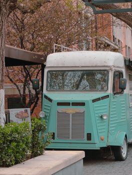 A vintage, mint-green food truck parked in an urban setting during springtime.