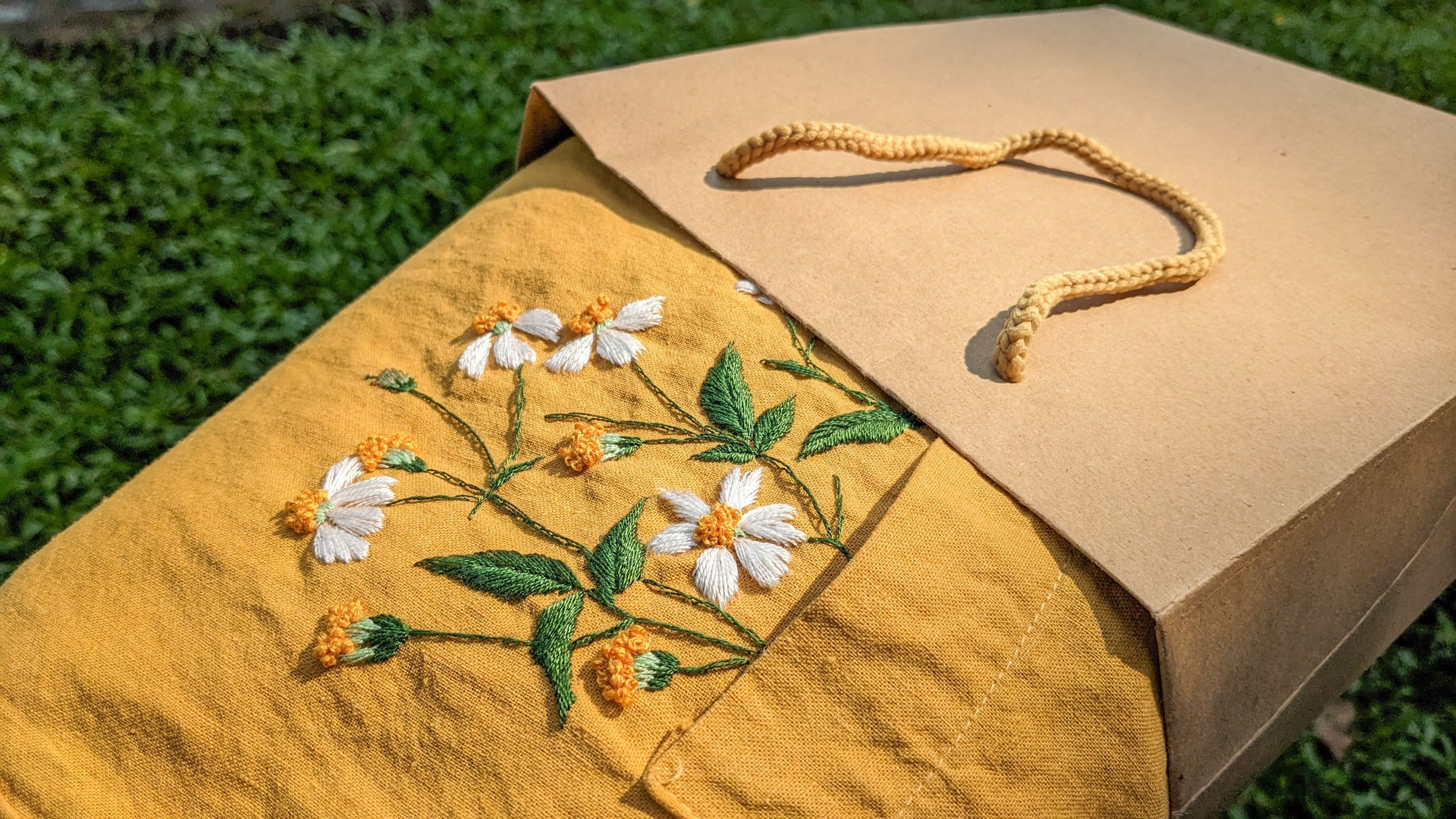 Close-up of delicate floral embroidery on mustard fabric, placed beside a paper gift bag. — Maynard Longarm Quilting