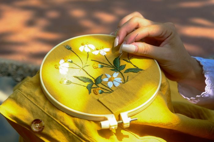 A woman hand-embroidering flowers on a yellow garment held in a hoop