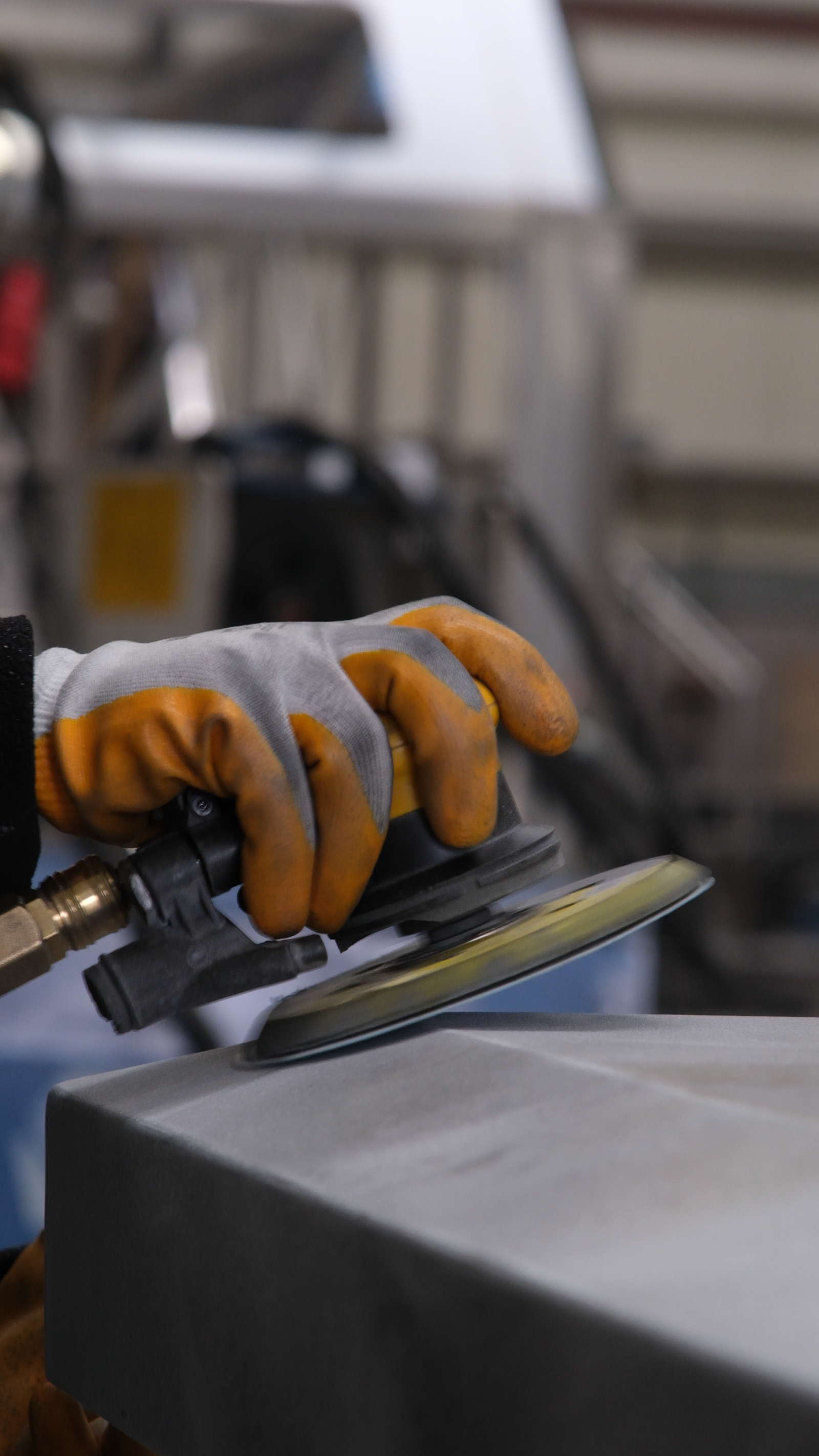 Worker smoothing a metal surface with a pneumatic sander in an industrial workshop