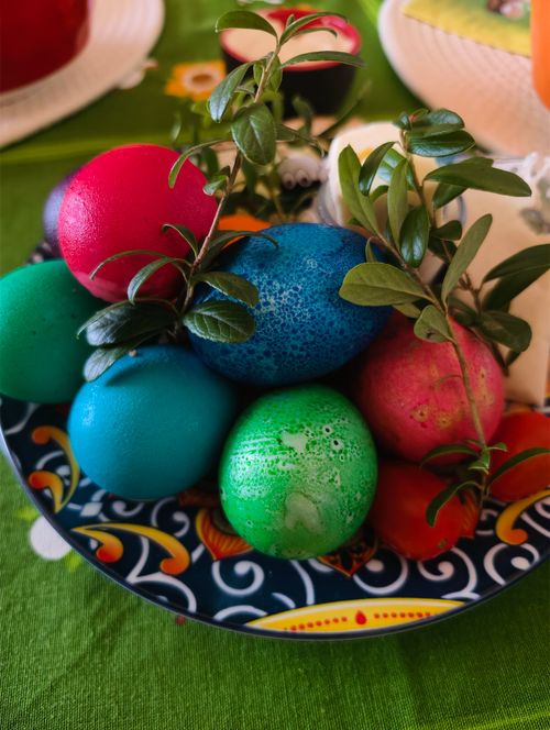 Free Vibrant Easter eggs with green sprigs on a decorative plate, perfect for seasonal celebrations. Stock Photo