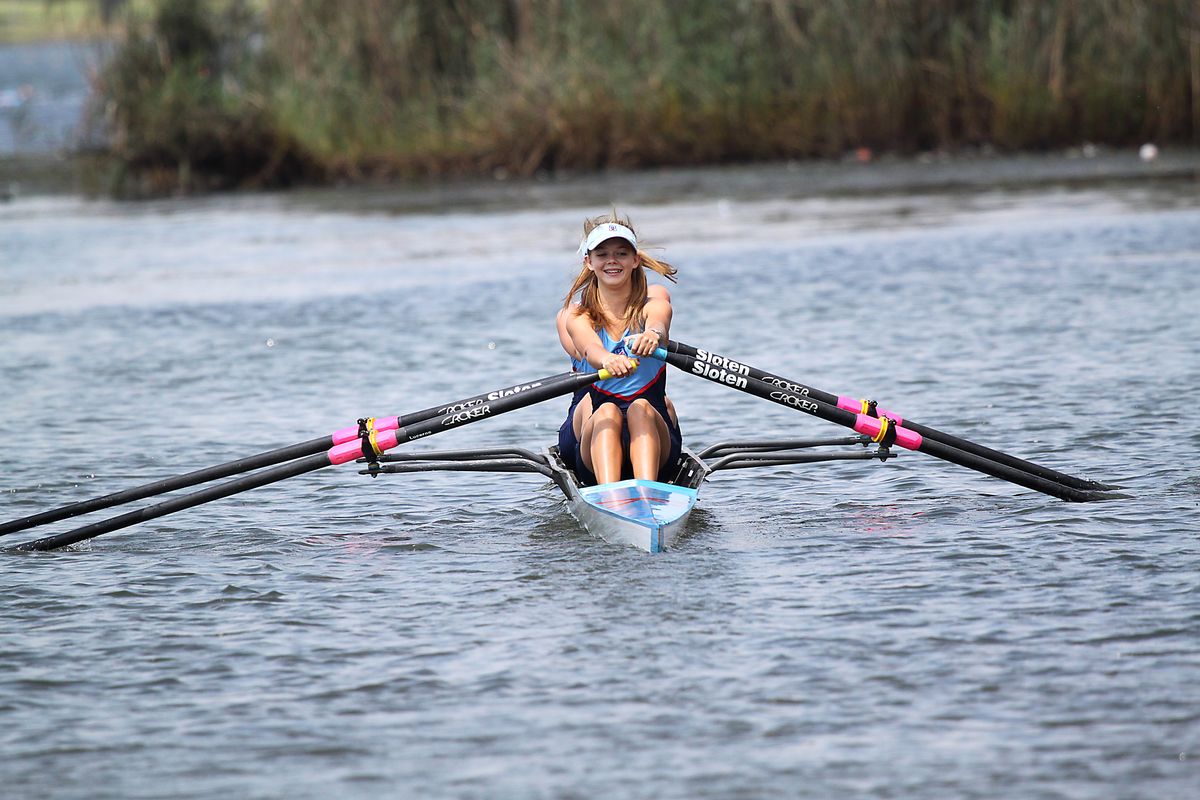 Smiling woman rowing a scull on a calm lake, enjoying outdoor water sports