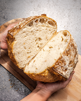 Close-up of freshly baked sourdough bread held by a baker, showcasing its texture and crust.
