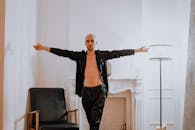 在现代室内环境中，一位秃头男子穿着时尚的黑色服装，双臂张开摆出姿势