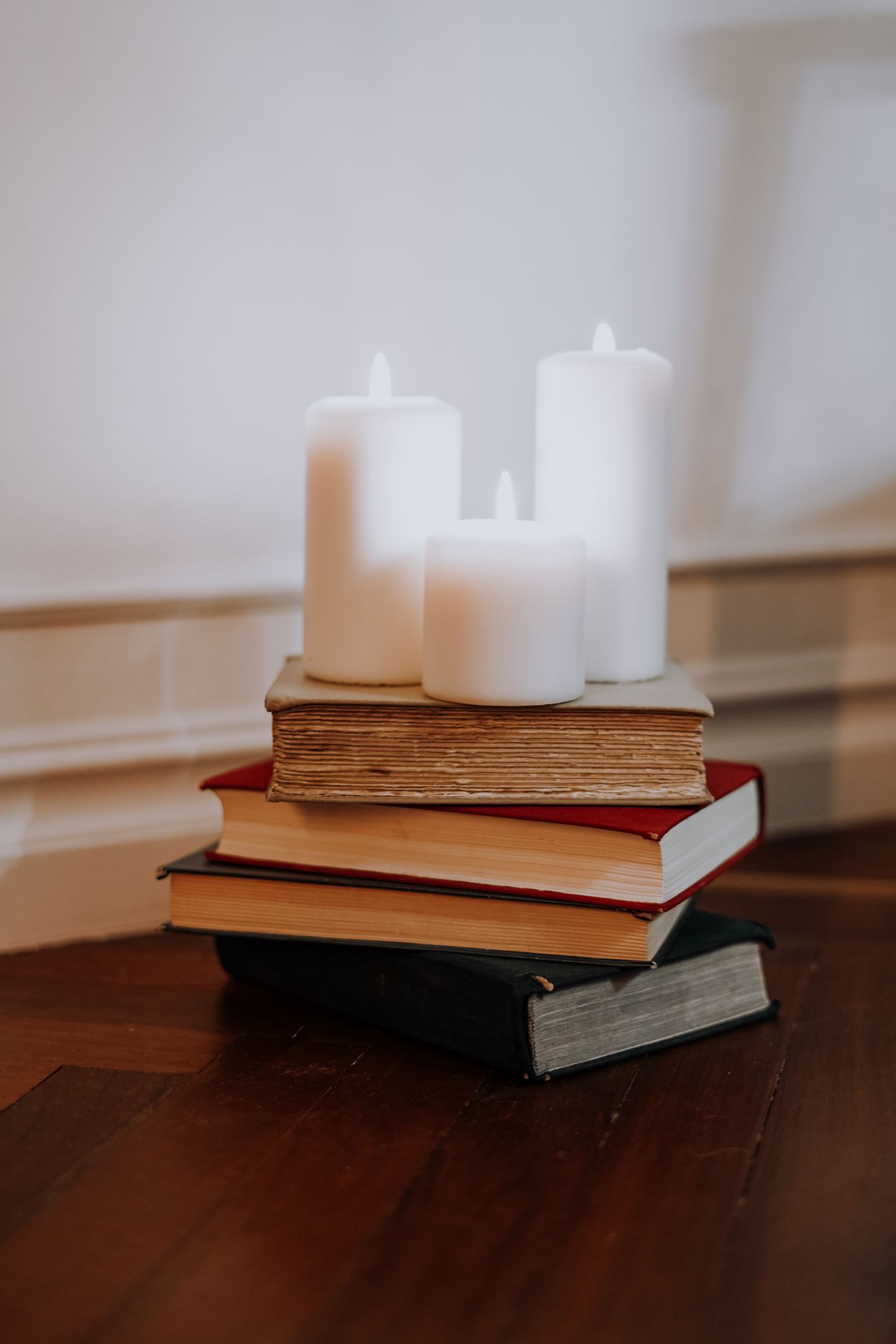 Three lit white candles standing on a stack of old books
