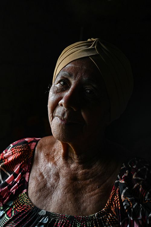 Free Emotive portrait of a senior woman with a pensive expression, wearing a colorful dress and headscarf. Stock Photo