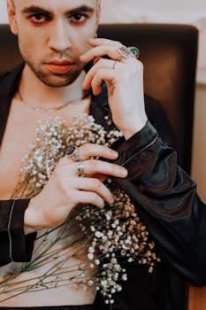 一位时髦的男人穿着黑色衬衫，戴着优雅的戒指，手里摆弄着精致的白花