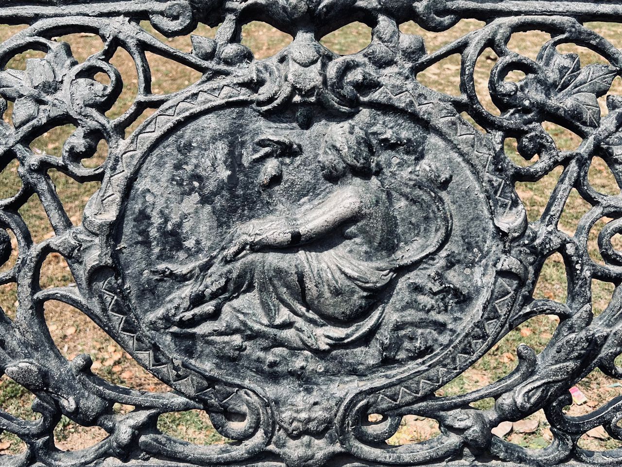 intricate design on a cast iron bench depicting a classical figure and