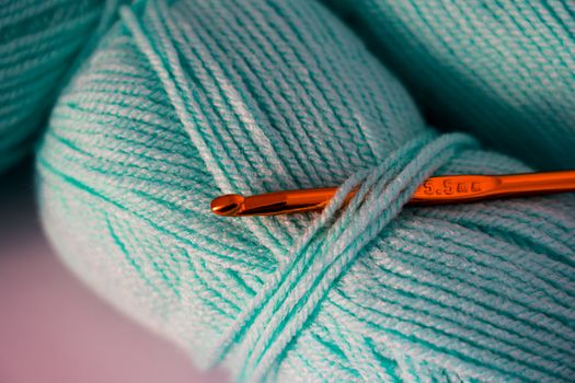 Macro photograph of teal yarn with a crochet hook, highlighting texture and detail.