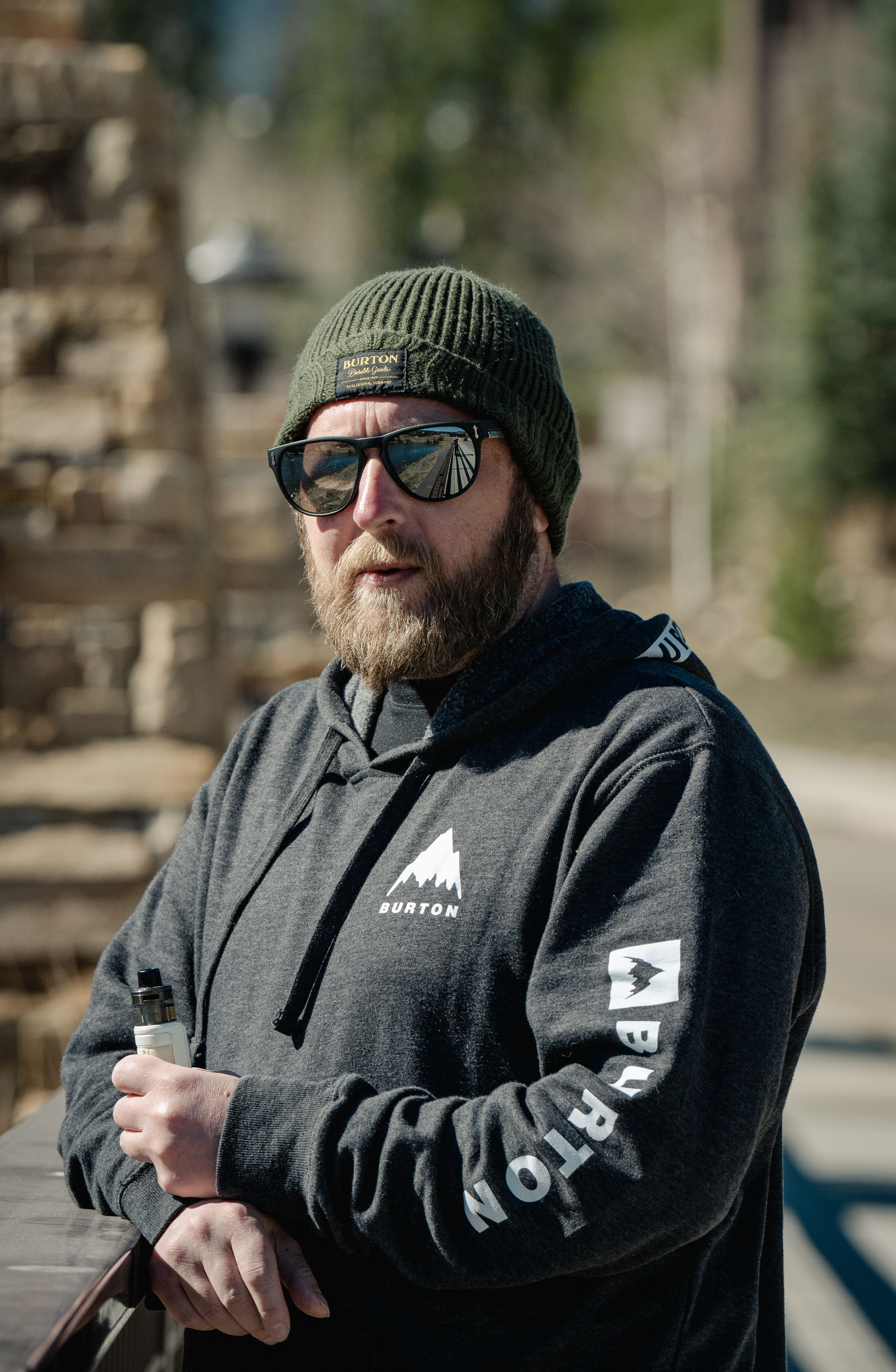 Man with a beard wearing sunglasses and a beanie enjoying a sunny day outdoors.