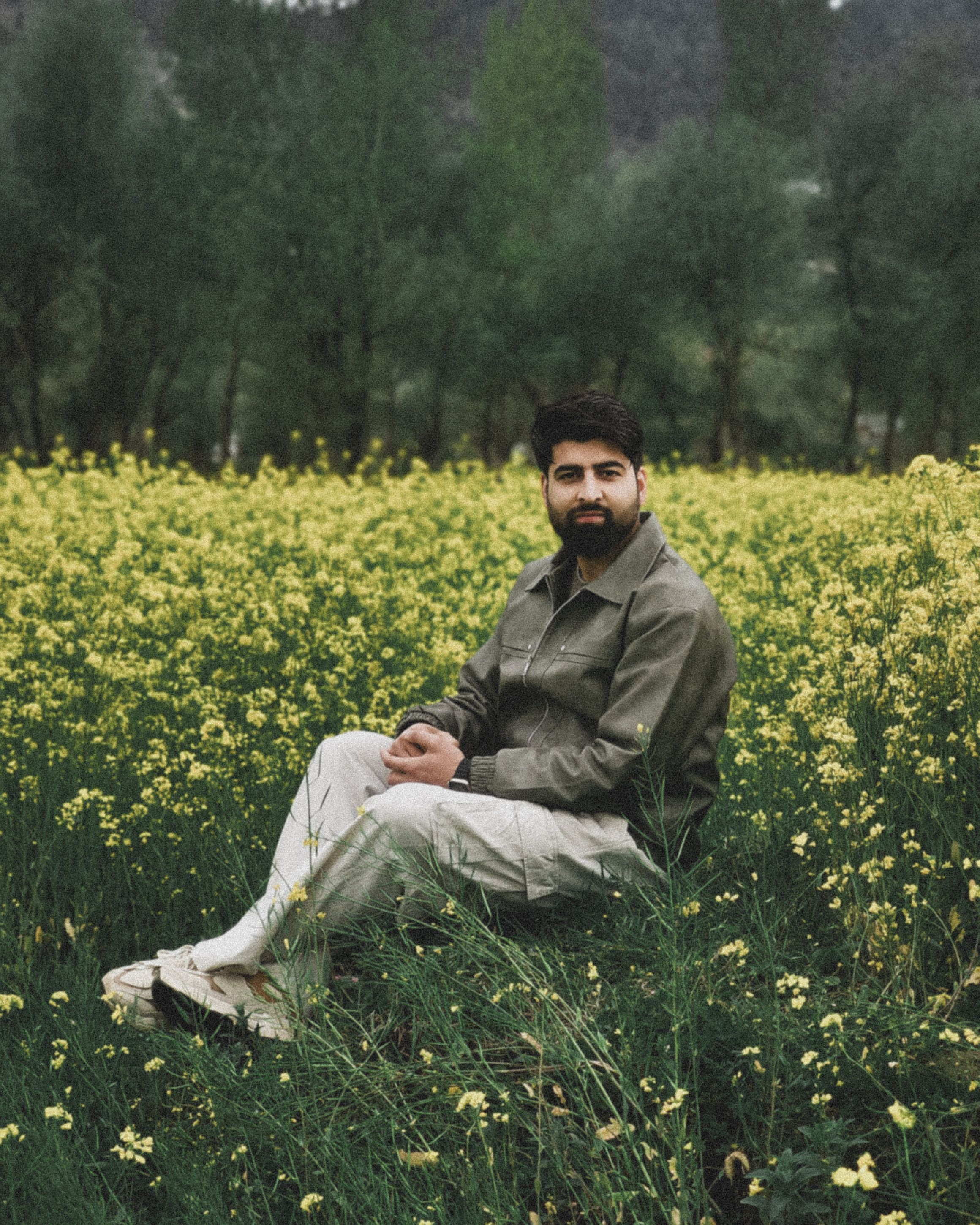 Man sitting in a lush field of yellow flowers, serene countryside scene.