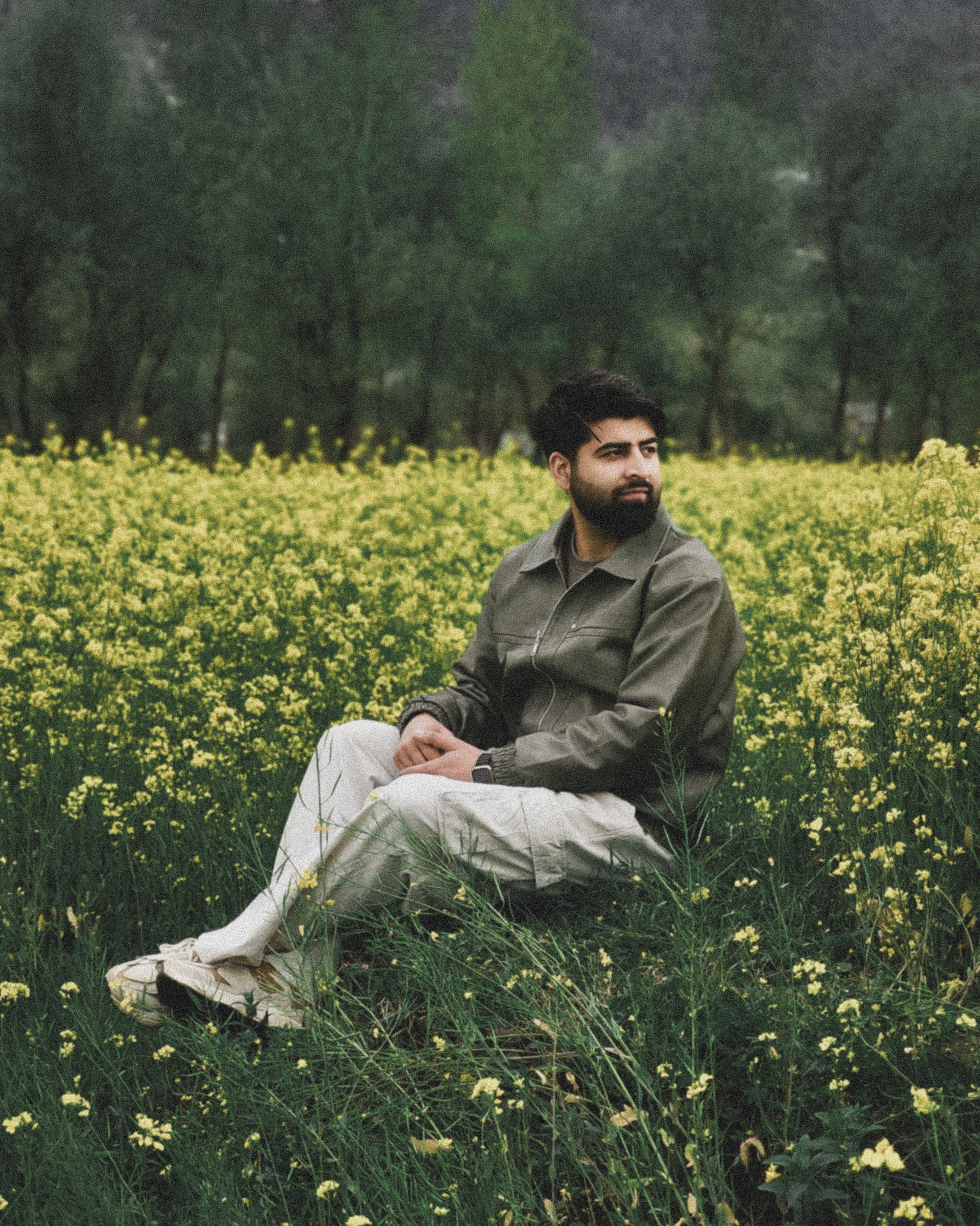 A man sitting peacefully in a vibrant mustard field surrounded by greenery.