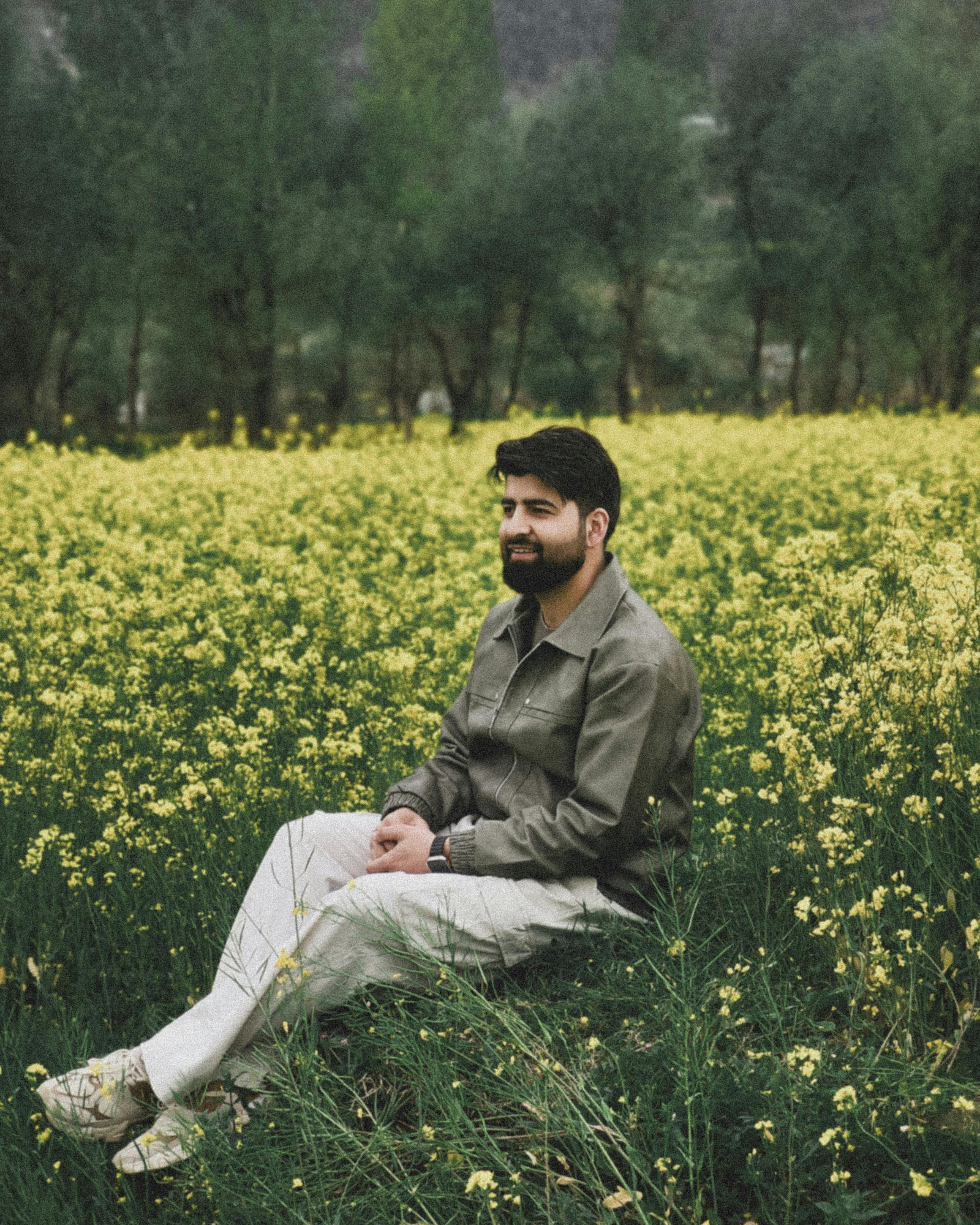 A man sitting in a peaceful yellow mustard field, surrounded by vibrant greenery.