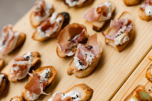 Free Close-up of gourmet crostini with prosciutto, ricotta, and sesame seeds on a wooden board. Stock Photo