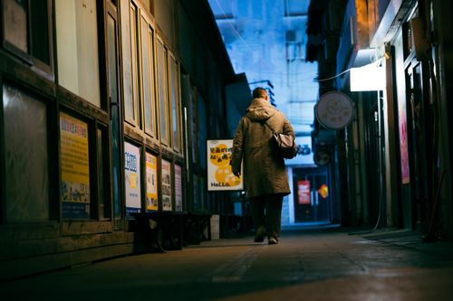 Free A solitary figure walks down a dimly lit alley in Qingdao, China, showcasing urban night life. Stock Photo