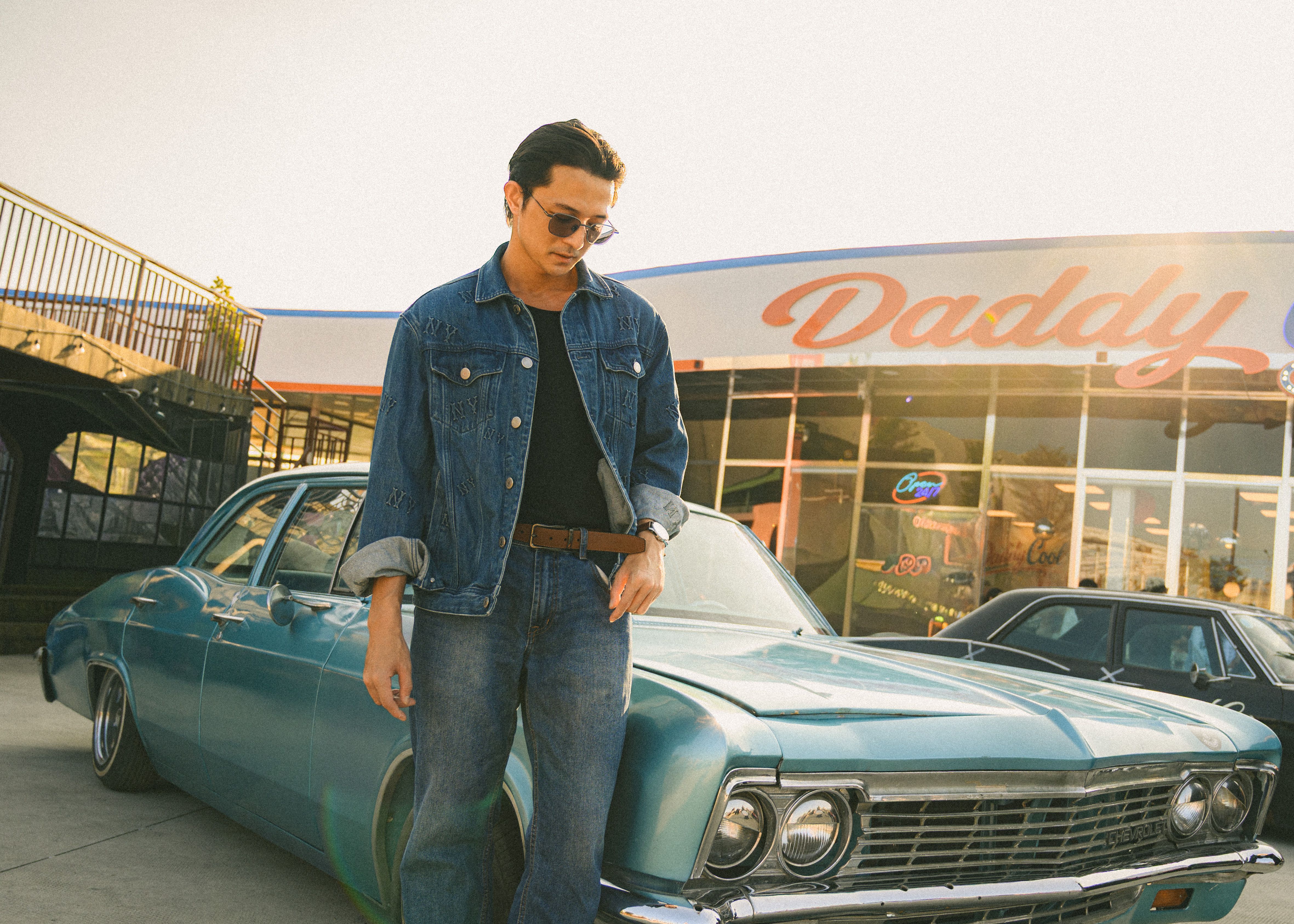 Young man in denim with vintage car and neon diner sign.