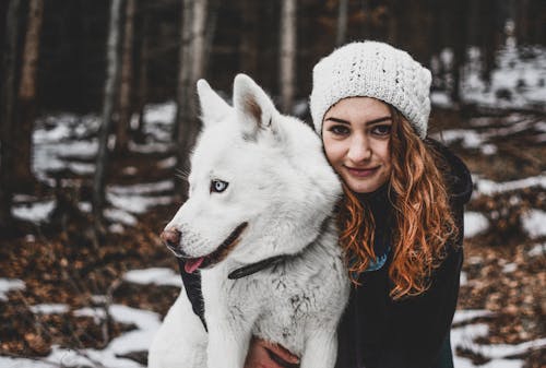 Mulher Usando Uma Touca De Malha Branca Enquanto Abraça Seu Husky Siberiano Branco