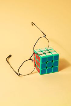 Eyeglasses rest on a Rubik's cube against a pastel background, showcasing a playful and modern concept.
