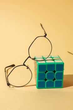 Stylish round eyeglasses resting on a colorful Rubik’s cube against a soft pastel background.