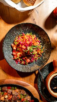 Colorful vegetable salad with cabbage, carrots, and mint in a stone bowl on a wooden table.