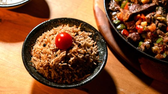 Dark bowl of vermicelli rice topped with a cherry tomato beside a meat stir-fry