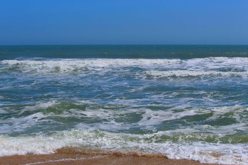 Free Vibrant ocean waves crashing on a sandy beach under a clear blue sky. Stock Photo