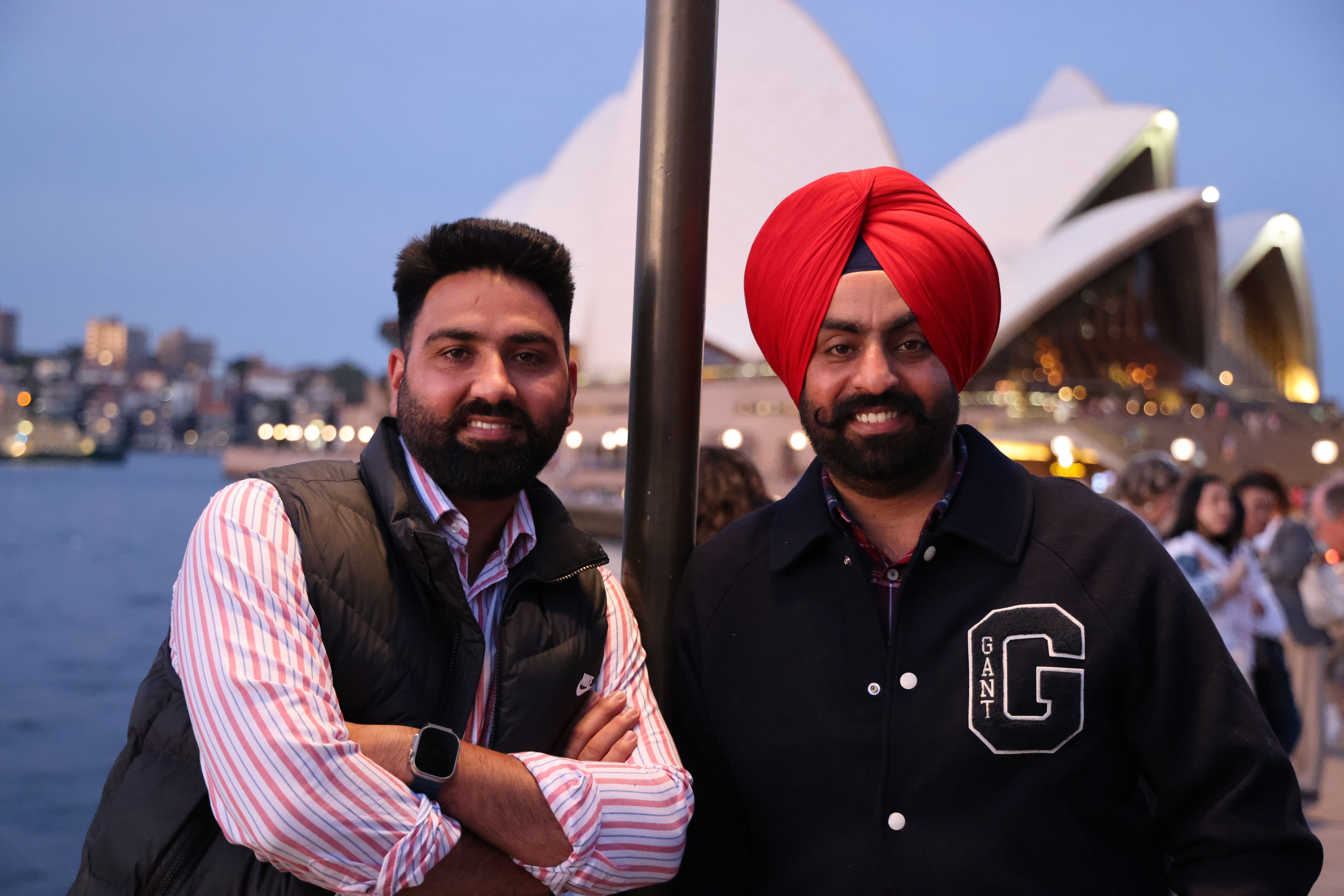 Two friends pose happily in front of the iconic Sydney Opera House at dusk.