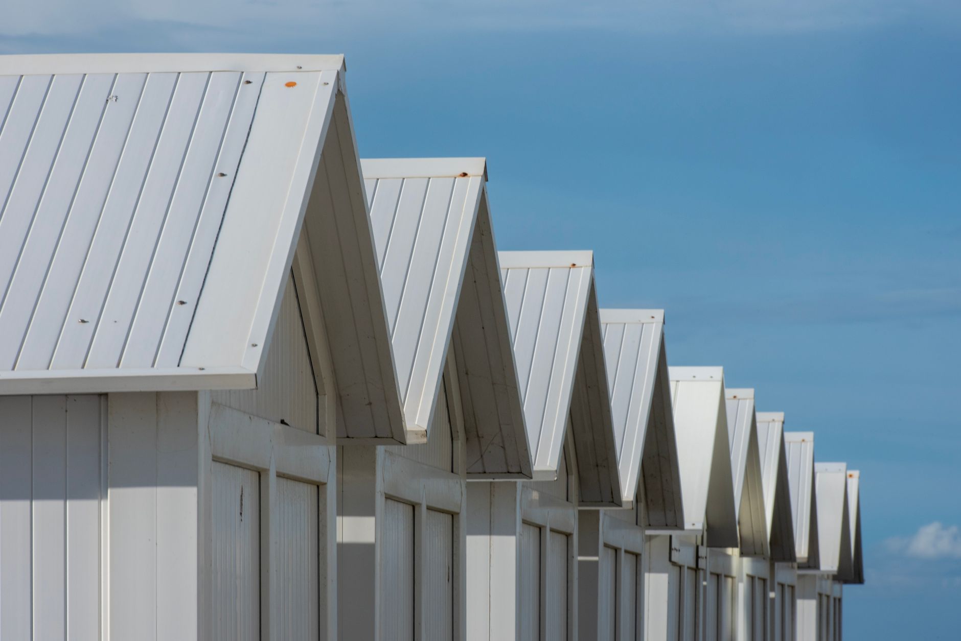 Row of minimalist beach huts with white roofs against a clear blue sky, perfect for summer themes.