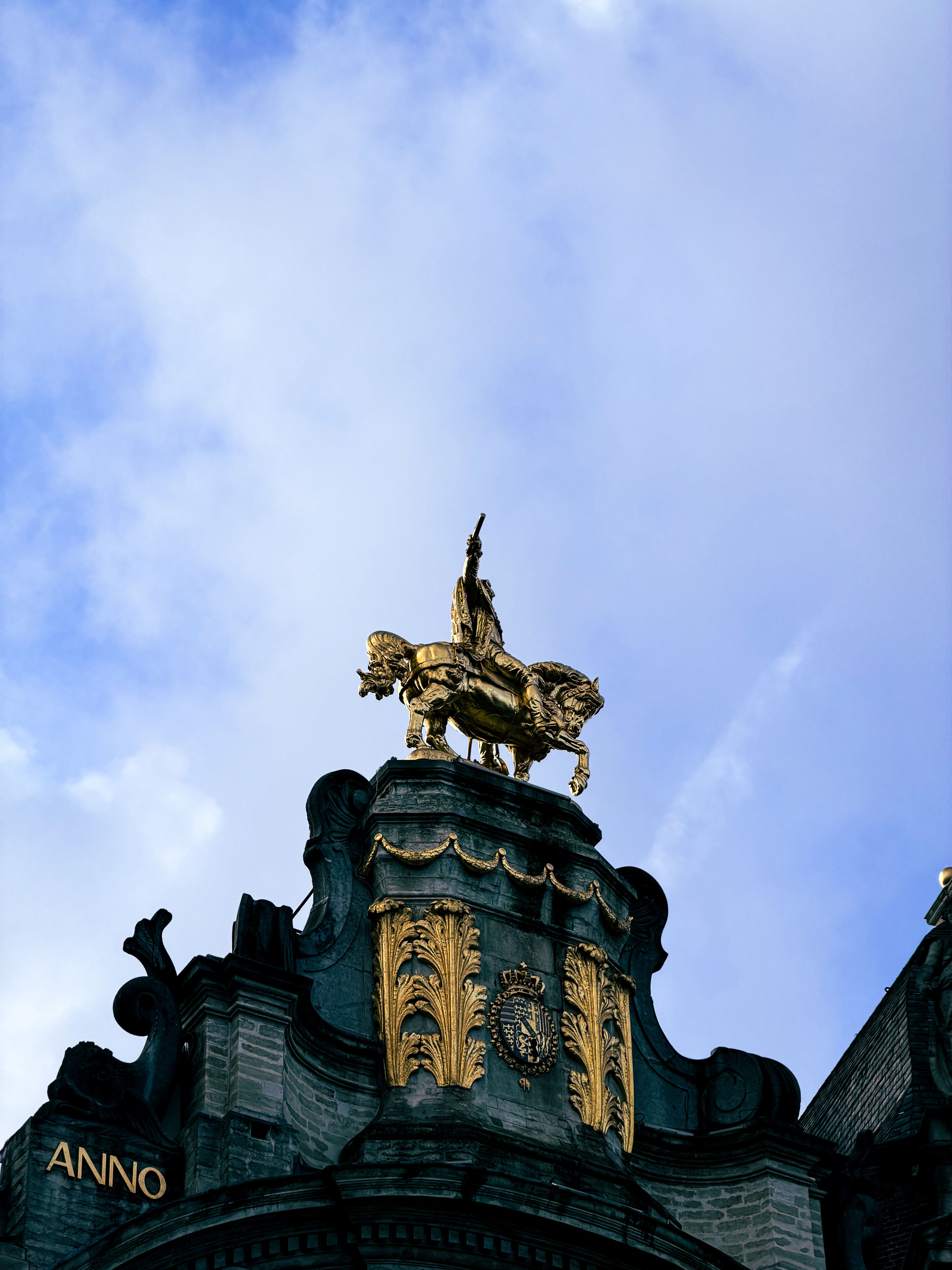 Dramatic view of a golden equestrian statue on a Grand Place building under blue skies in Brussels, Belgium.