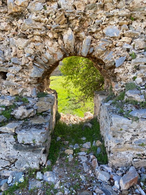 Free A scenic view through a stone archway in ancient ruins leading to greenery. Stock Photo