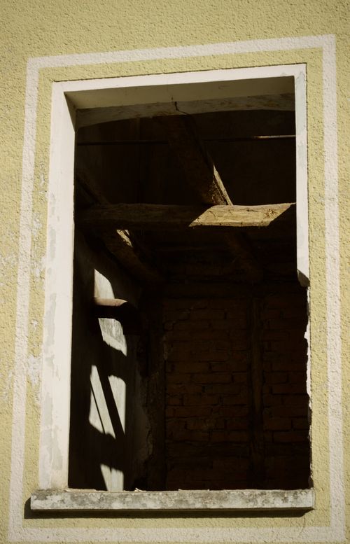 Free Sunlight casts shadows through a broken window frame, revealing an old brick wall inside. Stock Photo