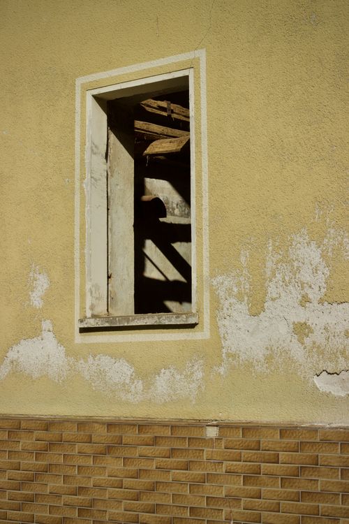 Free A vintage open window on a peeling yellow wall reveals shadows and textures, reminiscent of past architecture. Stock Photo