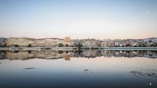 Free Scenic view of a city and its reflection in calm water at sunrise, creating a serene atmosphere. Stock Photo