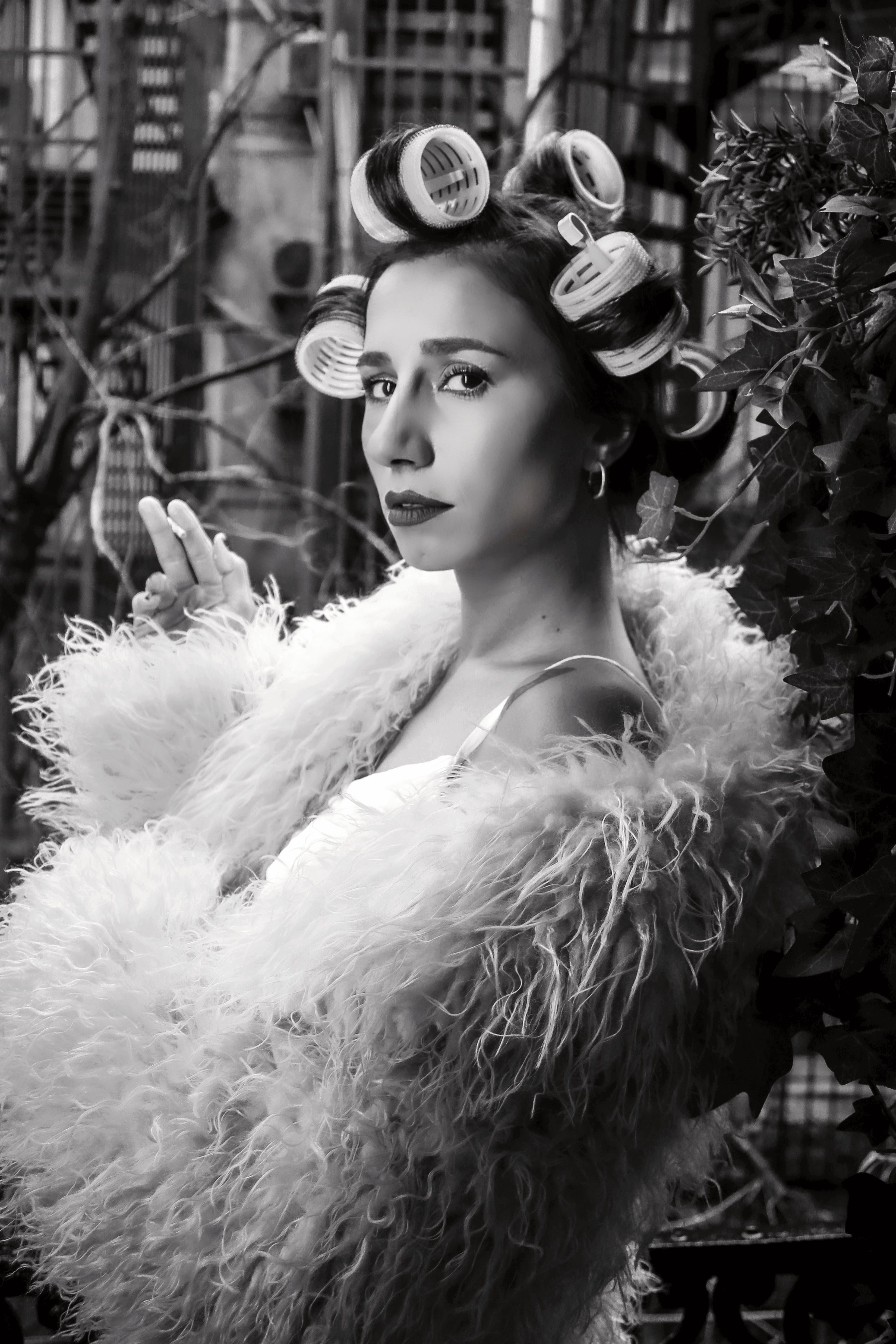 Stylish woman with hair rollers posing in a fluffy fur coat, urban outdoor setting.