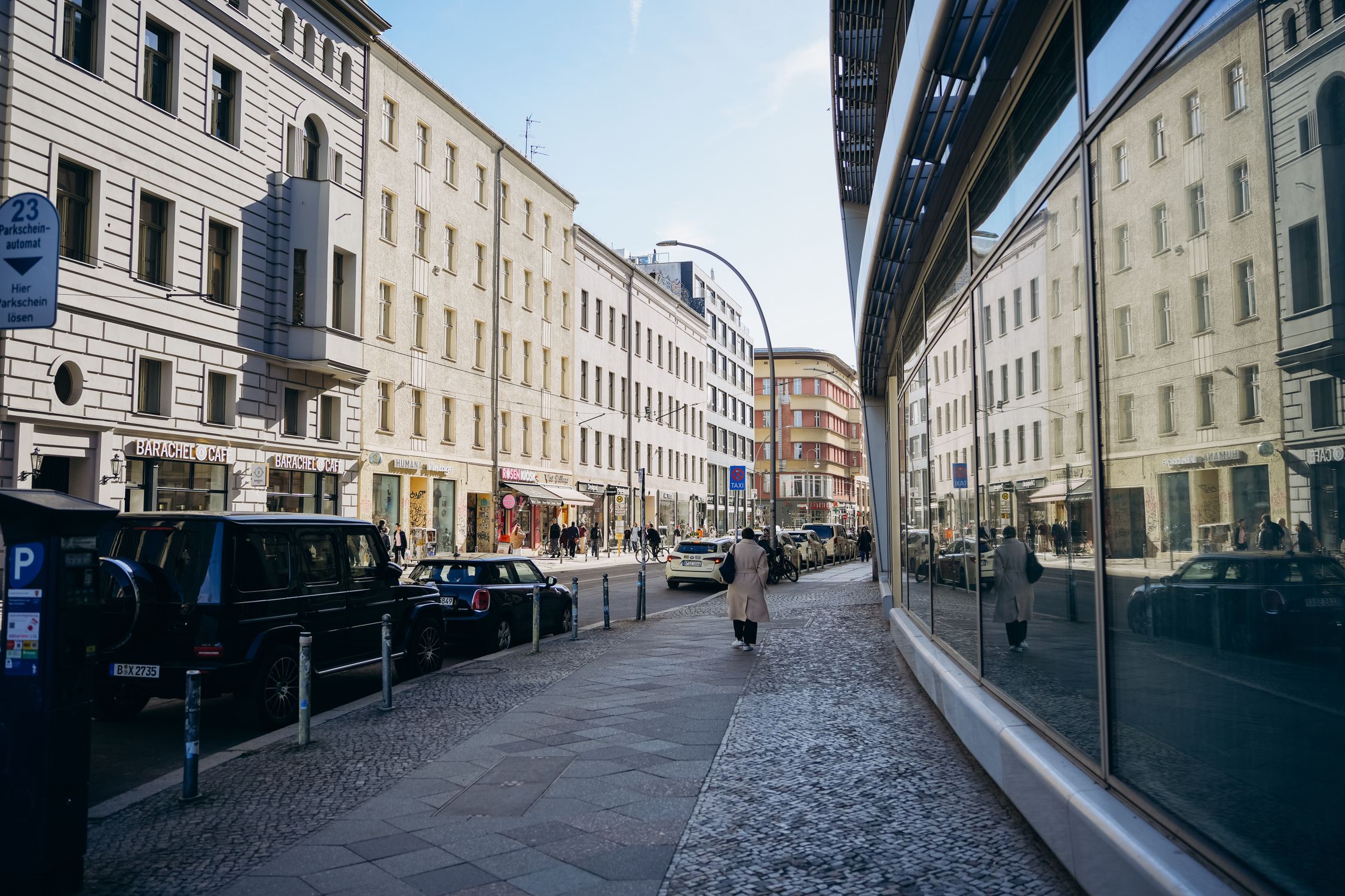 A bustling street in Berlin with modern and classic architecture reflecting on glass windows.