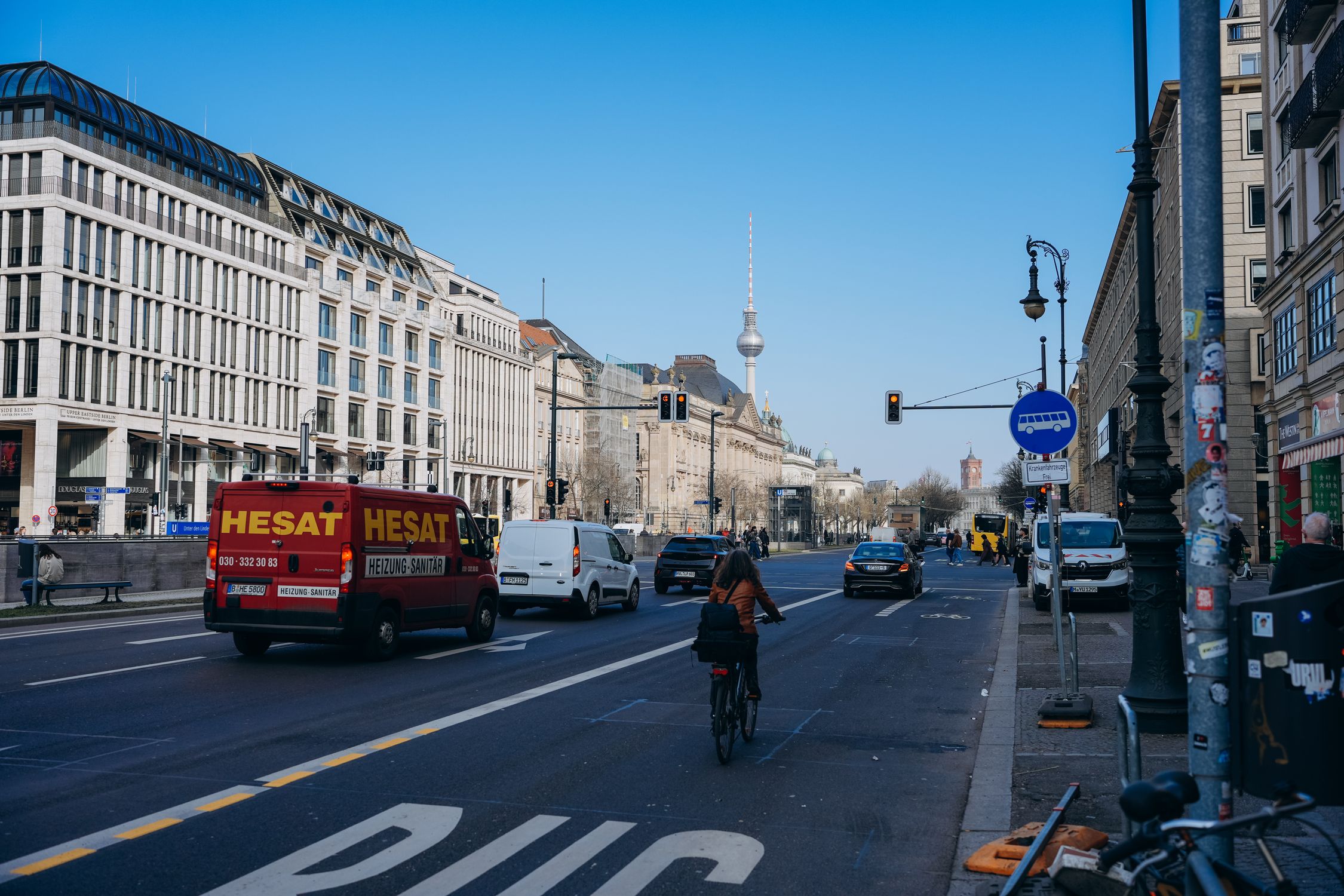 Berlin street view featuring a cyclist and iconic TV Tower under a clear blue sky.