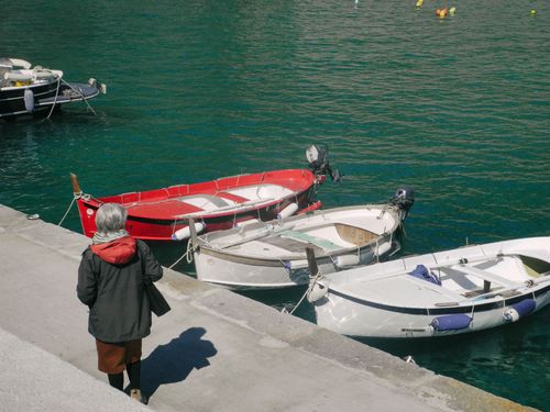 Free Elderly woman stands near dock watching colorful boats moored in serene marina. Stock Photo
