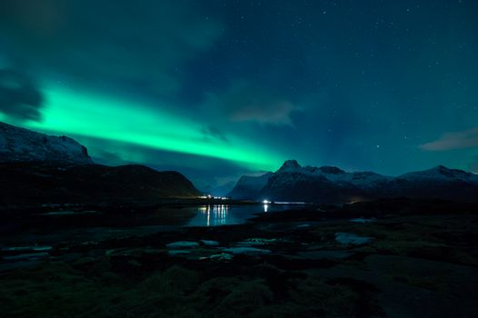 Breathtaking view of the Northern Lights illuminating snowy mountains and a serene lake in Nordland, Norway.