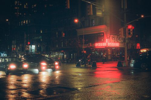 Free Glistening wet streets of NYC at night, featuring a vibrant oyster bar with red neon lights. Stock Photo