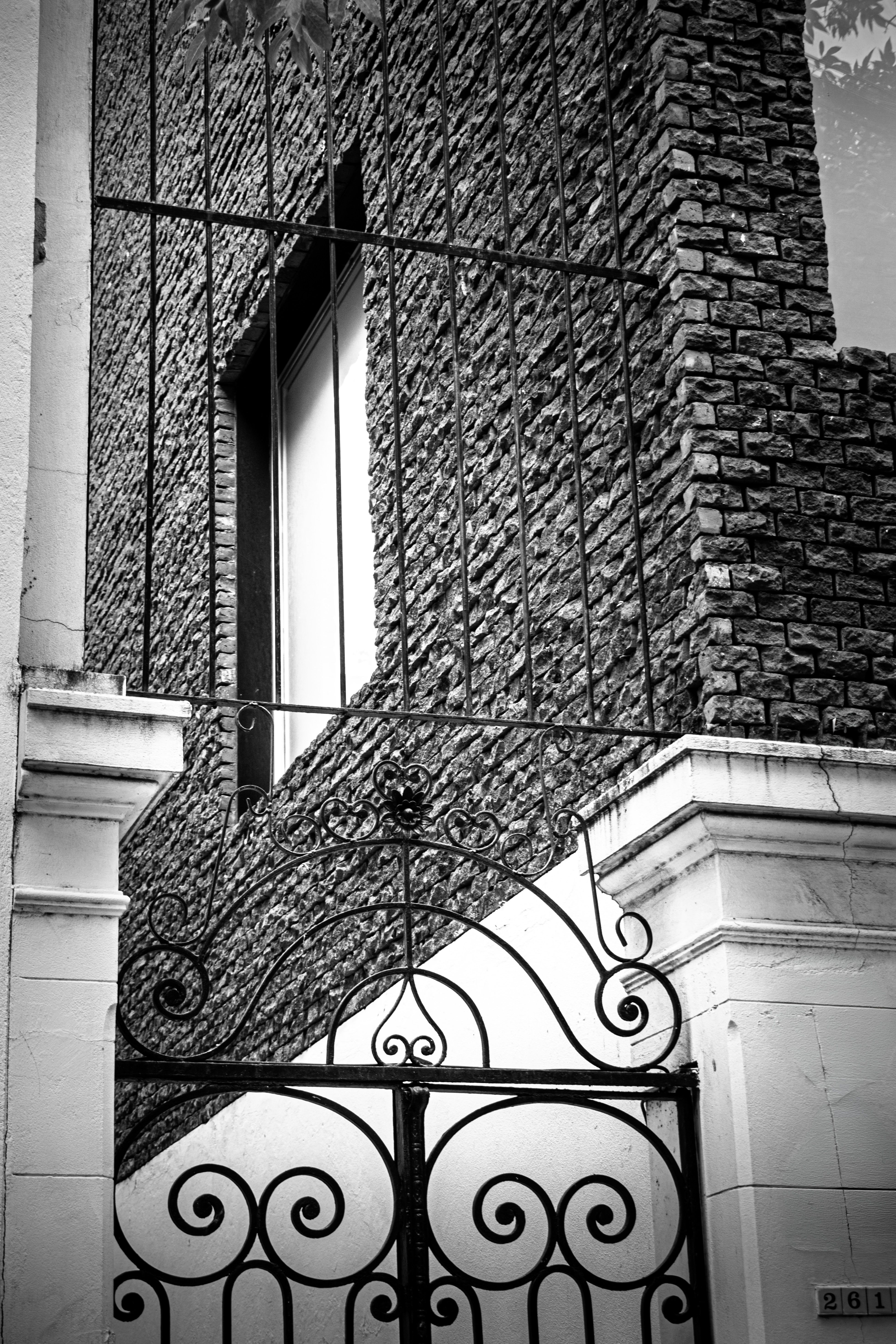 Black and white photo of an ornate iron gate set against a textured brick building facade.