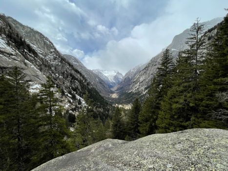 Breathtaking view of snow-capped mountains and lush forests in Val Masino, Italy.